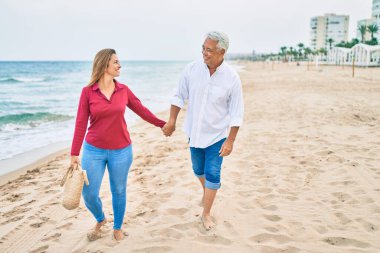 Orta yaşlı İspanyol çift kumsalda yürürken mutlu bir şekilde gülümsüyor..