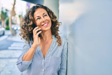 Orta yaşlı İspanyol kadın mutlu gülümsüyor ve şehirdeki akıllı telefondan konuşuyor..