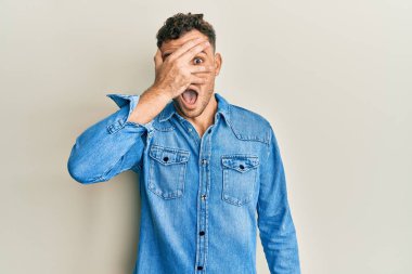 Gündelik kıyafetler giyen genç İspanyol adam şok içinde yüzünü ve gözlerini eliyle kapatıyor, parmaklarından korkuyla bakıyor. 