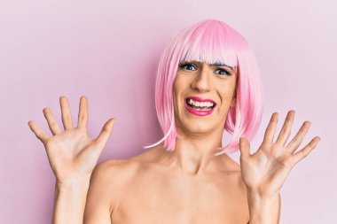 Pembe peruk takan genç adam korku ifadesinden korkuyor ve dehşete düşüyor. El hareketlerini bırak, şok içinde bağır. panik konsepti. 