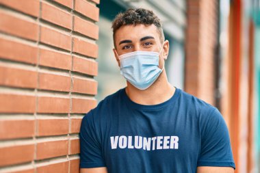 Şehirde duran tıbbi maske takan Latin kökenli gönüllü genç adam..