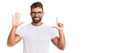 Gündelik kıyafetler giyen ve gözlük takan genç İspanyol adam yedi numaralı parmaklarını gösterip işaret ederken kendine güvenen ve mutlu bir şekilde gülümsüyor.. 