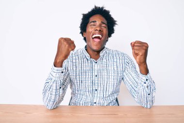 Yakışıklı Afro saçlı, sıradan kıyafetler giyen, mutlu ve heyecanlı, kollarını kaldırıp, gülümseyen ve başarı için bağıran Afro-Amerikan erkeği. kutlama konsepti. 