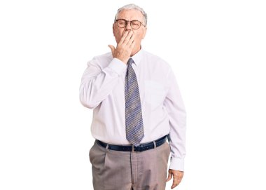 İş kıyafetleri giyen yaşlı, gri saçlı bir adam ağzını eliyle kapatmaktan sıkılmış. Huzursuz ve uykulu.. 