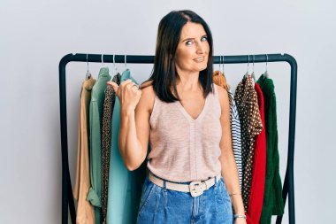 Orta yaşlı esmer kadın profesyonel alışverişçi olarak çalışıyor. Gülümsüyor, gülümsüyor ve başparmağını kaldırarak yüzünü işaret ediyor.. 