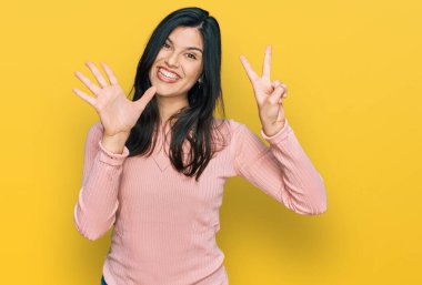 Genç İspanyol kadın gündelik kıyafetler giyer ve yedinci parmaklarını göstererek gülümseyerek mutlu ve kendinden emin bir şekilde gösterir.. 