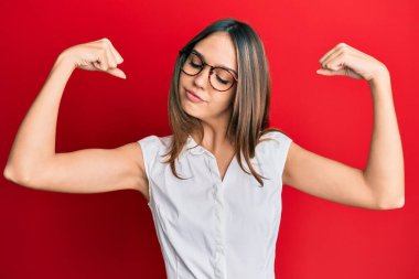 Sıradan kıyafetler ve gözlük takan genç esmer kadın gururla gülümseyen kol kaslarını gösteriyor. fitness konsepti. 