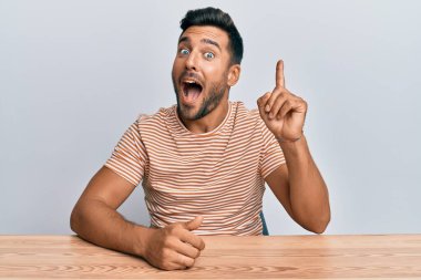 Gündelik giysiler giyen yakışıklı İspanyol adam masaya oturmuş başarılı bir fikirle işaret ediyor. Heyecanlı ve mutlu. Bir numara.. 