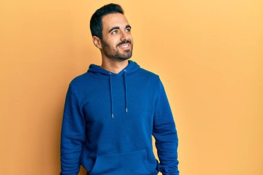 Gündelik kıyafetler giyen genç İspanyol bir adam yüzünde gülümsemeyle yan yana bakıyor, doğal bir ifade. Kendinden emin gülen. 