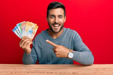 Yakışıklı İspanyol adam İsviçre frangı tutuyor. Gülümsüyor, mutlu bir şekilde parmakla işaret ediyor. 