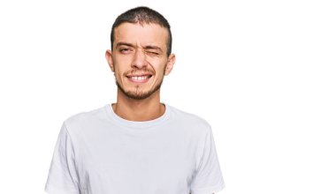 Latin asıllı beyaz tişört giyen genç adam kameraya seksi bir ifadeyle bakıyor, neşeli ve mutlu bir yüzle.. 