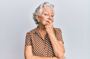 Üstün gri saçlı, günlük kıyafetler giyen, kameraya kendinden emin, kolları çapraz ve çenesi kalkık gülümseyen bir kadın. Olumlu düşünmek. 