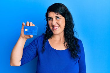 Artı, elinde kredi kartı tutan esmer kadın pozitif ve mutlu görünüyor ve gülümsüyor, kendine güvenen bir gülümsemeyle dişlerini gösteriyor. 