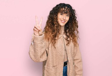 Kışlık giysiler giyen genç İspanyol kız kendini beğenmiş ve mutlu bir şekilde gülümserken iki numarayı işaret ediyor.. 