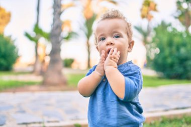 Üzgün küçük çocuk, güneşli bir günde parkta diş etlerine dokunduğu için parmaklarını dudaklarına koyuyor. Güzel sarı saçlı erkek bebek yeni bebek dişleri için acı çekiyor.