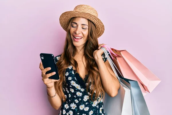 Young brunette woman holding shopping bags and smartphone smiling and laughing hard out loud because funny crazy joke.