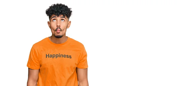 年轻的阿拉伯男子穿着印有快乐词信息的T恤衫 用嘴唇 疯狂和滑稽的姿势做鬼脸 有趣的表达方式 — 图库照片