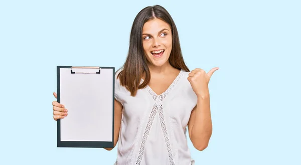 Young Caucasian Woman Holding Clipboard Blank Space Pointing Thumb Side — Stock Photo, Image