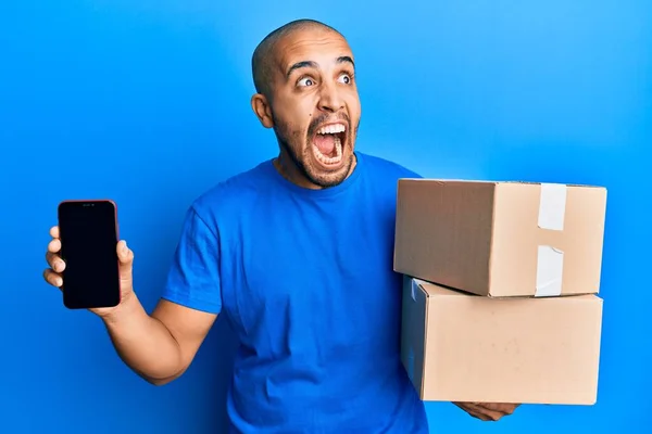 Hispanic Adult Man Holding Delivery Packages Showing Smartphone Screen Angry — Stock Photo, Image