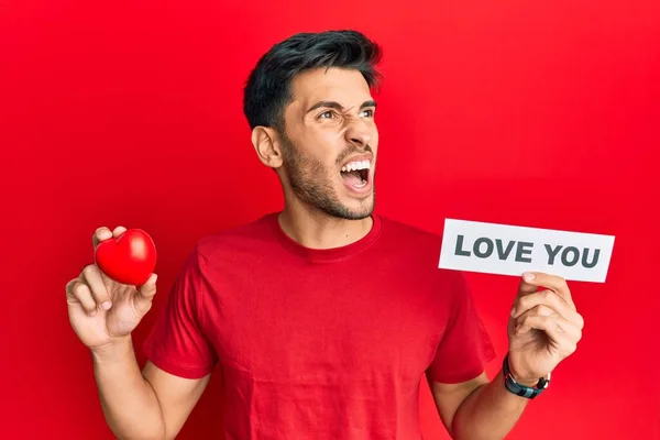 Jovem Homem Bonito Segurando Coração Vermelho Amo Mensagem Irritado Louco — Fotografia de Stock