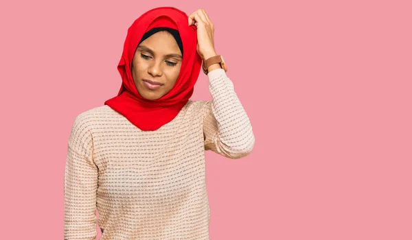 身穿传统伊斯兰头巾的年轻的非洲裔美国女人对问题感到困惑和疑惑 拿不定主意 手拿着头思考 沉思的概念 — 图库照片