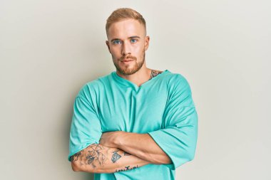 Gündelik kıyafetler giyen, kuşkucu ve gergin genç beyaz bir adam. Yüzünde çapraz kollarla onaylamayan bir ifade var. negatif kişi. 
