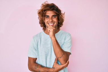 Gündelik kıyafetler giyen genç İspanyol adam kameraya bakıyor kollarını kavuşturup gülümseyerek ve çenesini kaldırarak. Olumlu düşünmek. 