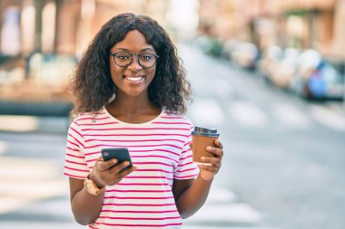 Genç Afrikalı Amerikalı kız akıllı telefon kullanıyor. Şehirde kahve içiyor..