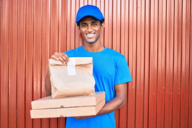 Kurye üniforması giyen Afrikalı kurye dışarıda yiyecek tutuyor.