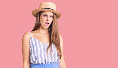 Şok olmuş yüzüne yaz şapkası takan genç, güzel sarışın kadın şüpheci ve alaycı görünüyor, ağzı açık kalınca şaşırıyor. 