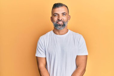 Yüzünde mutlu ve havalı bir gülümseme olan sıradan beyaz tişört giyen orta yaşlı yakışıklı bir adam. şanslı kişi. 