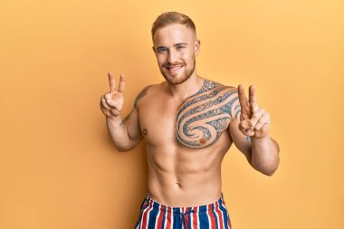 Mayo giyen genç beyaz adam kameraya bakıp zafer işareti yaparken gülümsüyor. İki numara.. 