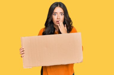 Güzel esmer bir kadın, elinde boş bir karton pankart tutuyordu. Ağzı eliyle kaplayan boş pankart, şok olmuş ve hata yapmaktan korkuyordu. şaşırmış ifade 