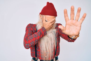 Gri saçlı, uzun sakallı, hippi görünümlü, elleri yün şapkalı, üzgün ve korku ifadeli yaşlı bir adam. utangaç ve olumsuz kavram. 