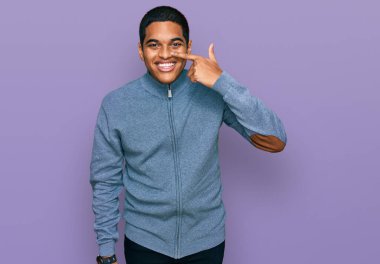 Gündelik kazak giyen genç, yakışıklı İspanyol adam, el ve yüz parmaklarını göstererek, neşeli bir şekilde gülümsüyor. güzellik konsepti 