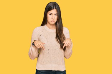 Kış süveteri giyen genç esmer kadın üzgün ve üzgün görünüyor, parmaklarıyla yönü gösteriyor, mutsuz ve depresif.. 