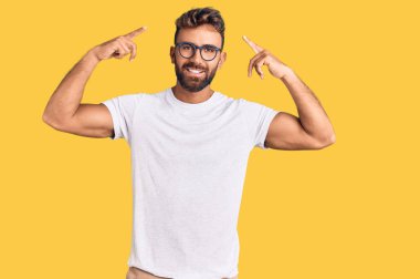 Gündelik kıyafetler giyen ve gözlüklü genç adam iki eliyle başını gösteren gülümseme, harika fikir ya da düşünce, iyi hafıza 