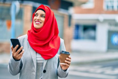 Genç Arap iş kadını akıllı telefon kullanıyor ve şehirde kahve içiyor..