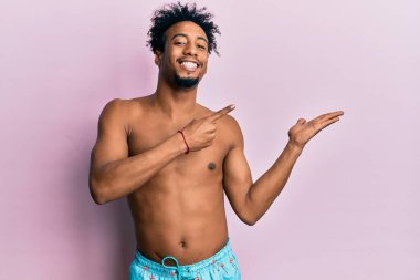 Sakallı Afrikalı genç bir Amerikalı mayo giyip kameraya hayret ediyor ve gülümsüyor.. 