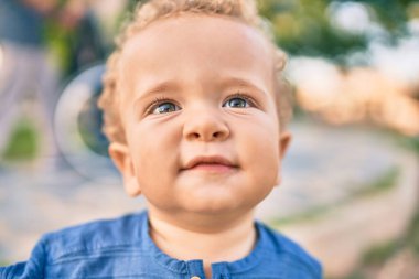 Sevimli ve mutlu küçük çocuk güneşli bir günde parkta eğleniyor. Güzel sarı saçlı erkek çocuk dışarıda oynuyor.