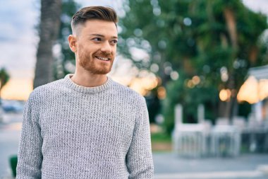 Genç beyaz adam gülümseyerek şehirde mutlu mesut duruyor..