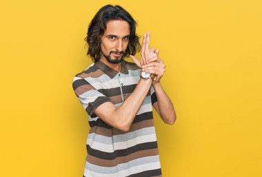 Latin asıllı genç adam gündelik giysiler giyiyor. Elinde sembolik bir silah var. El hareketleriyle cinayet silahlarıyla oynuyor. 