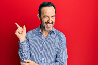 Orta yaşlı, sıradan kıyafetler giyen, yüzünde kocaman bir gülümseme olan, elleri ve parmaklarıyla kameraya bakan İspanyol bir adam.. 