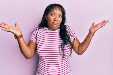 Orta yaşlı Afro-Amerikalı kadın, gündelik giysiler giyiyor, habersiz ve kolları açık, hiçbir fikrim yok ve şüpheli bir yüz var.. 