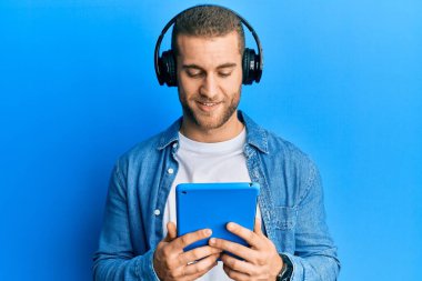 Kulaklık takan genç, beyaz bir adam pozitif ve mutlu görünüyor. Kendine güvenen bir gülümsemeyle dişlerini gösteriyor. 