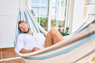 Yakışıklı beyaz adam mutlu bir şekilde gülerek terasta dinleniyor.