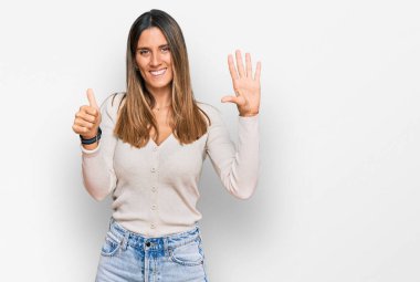 Gündelik kıyafetler giyen genç bir kadın altı numarayı gösterip işaret ederken kendinden emin ve mutlu bir şekilde gülümsüyor.. 