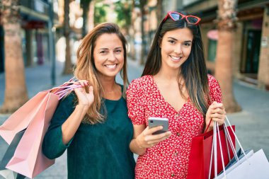 Güzel İspanyol anne ve kızı akıllı telefon kullanıyor ve şehirde alışveriş yapıyor..