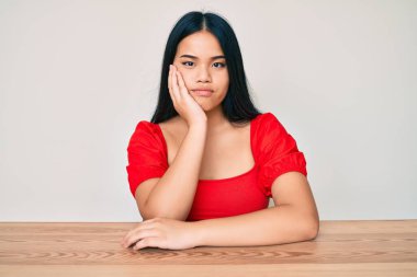 Genç, güzel Asyalı bir kız, sıradan kıyafetler giyip masaya oturuyor. Kollarını kavuşturup depresyondan sıkılmış ve yorgun görünüyor.. 