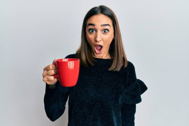 Genç esmer kız bir fincan kahve içiyor. Korkmuş ve ağzı açık kalmış, şaşırmış ve şaşırmış. 